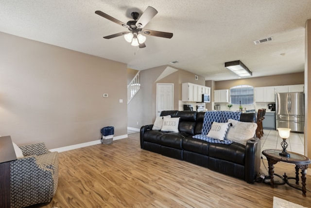 living room with visible vents, baseboards, ceiling fan, a textured ceiling, and light wood finished floors