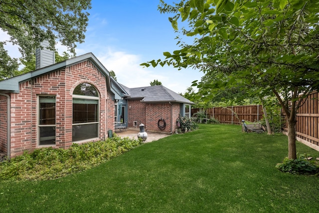 rear view of property with brick siding, a fenced backyard, a chimney, a patio, and a yard