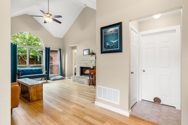interior space with a ceiling fan, visible vents, a fireplace, light wood-type flooring, and high vaulted ceiling