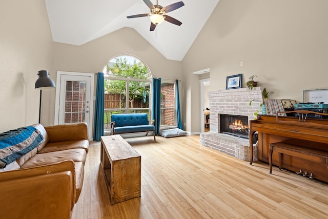 living room with a brick fireplace, a ceiling fan, light wood-style flooring, and lofted ceiling