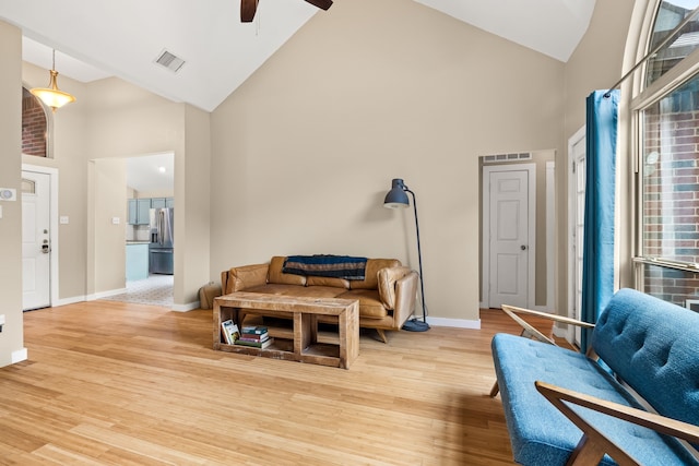 living area featuring ceiling fan, visible vents, high vaulted ceiling, baseboards, and light wood-style flooring