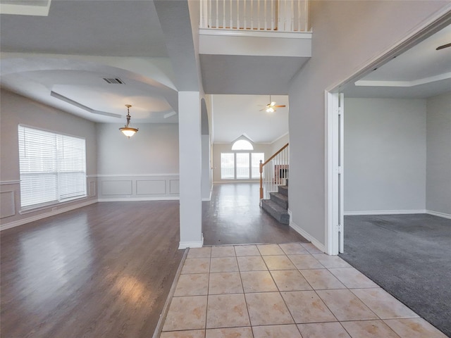 tiled foyer featuring a ceiling fan, visible vents, stairway, baseboards, and a tray ceiling