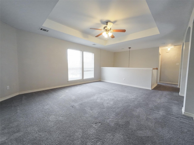 unfurnished room with a ceiling fan, visible vents, baseboards, a tray ceiling, and dark carpet