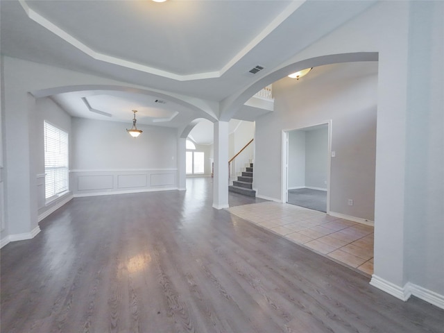 unfurnished living room featuring stairs, arched walkways, wood finished floors, and a raised ceiling