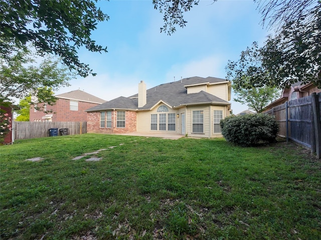 rear view of house featuring a fenced backyard, a chimney, a yard, and brick siding