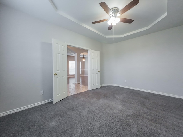 carpeted spare room featuring baseboards, ceiling fan, a tray ceiling, and tile patterned floors