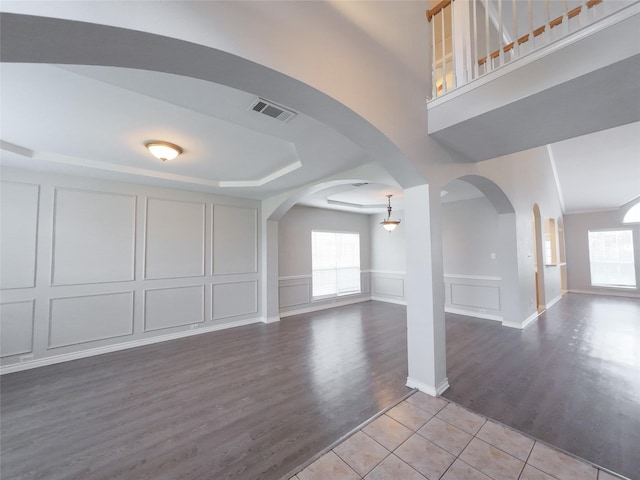 interior space featuring visible vents, arched walkways, wood finished floors, baseboards, and a decorative wall