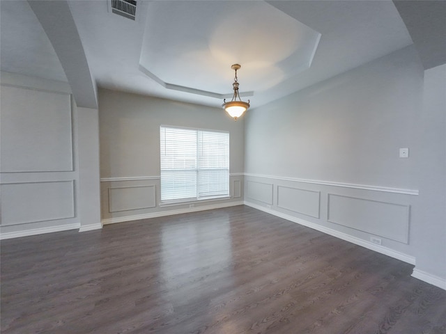 empty room featuring wainscoting, a raised ceiling, a decorative wall, dark wood finished floors, and visible vents