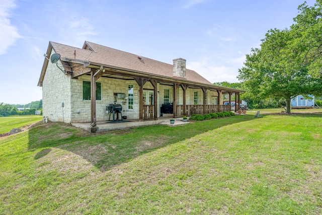 rear view of house featuring roof with shingles, a patio, a yard, and stone siding