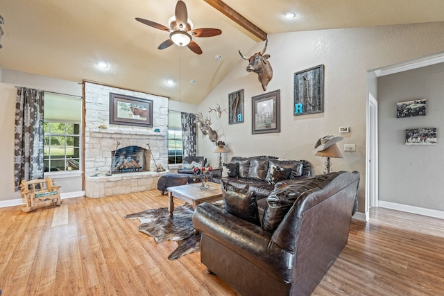 living room with a ceiling fan, a stone fireplace, wood finished floors, baseboards, and lofted ceiling with beams