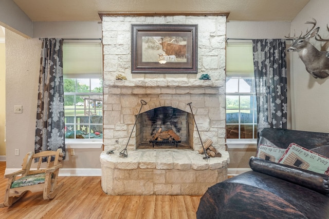 living area with baseboards, a stone fireplace, wood finished floors, and a wealth of natural light