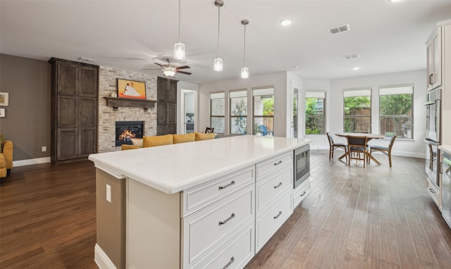 3004 Culver Ave, Celina, TX 75009 - kitchen with a brick fireplace, a ceiling fan, stainless steel microwave, dark wood-type flooring, and visible vents