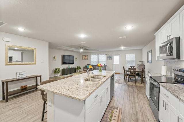 kitchen featuring stainless steel appliances, white cabinetry, a sink, and light wood finished floors