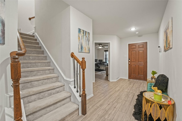 foyer entrance featuring stairs, a ceiling fan, baseboards, and light wood-style floors