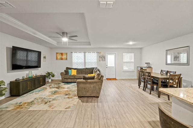 living area with visible vents, ceiling fan, a tray ceiling, and light wood-type flooring