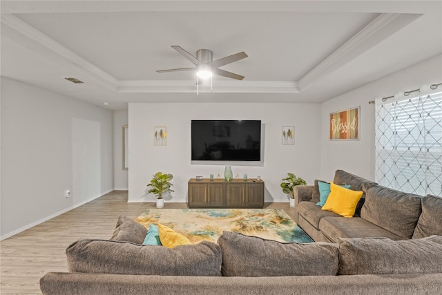 living area with ceiling fan, visible vents, light wood-type flooring, baseboards, and a tray ceiling