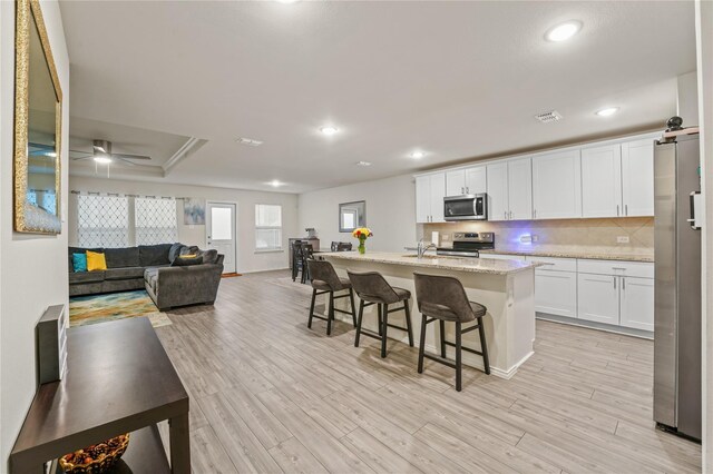 kitchen featuring white cabinets, stainless steel appliances, visible vents, and a kitchen breakfast bar