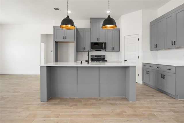 kitchen featuring tasteful backsplash, gray cabinetry, light countertops, a sink, and stainless steel appliances
