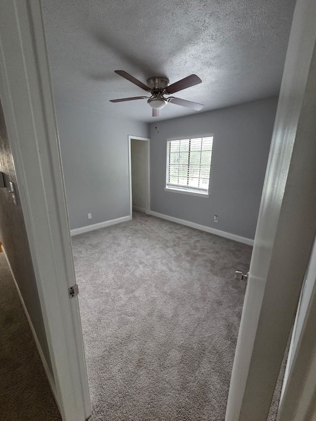 unfurnished room with carpet floors, a textured ceiling, baseboards, and ceiling fan