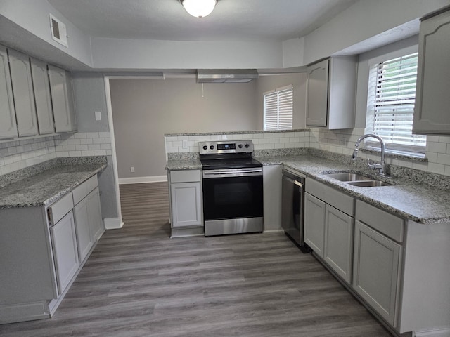 kitchen with a sink, appliances with stainless steel finishes, backsplash, and wood finished floors