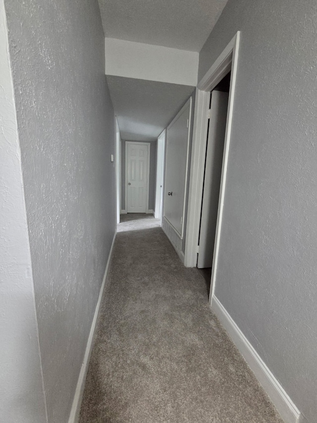hallway featuring carpet flooring, baseboards, and a textured wall