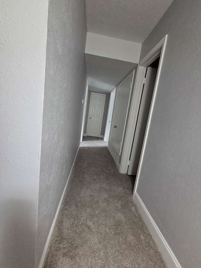 hall featuring carpet floors, a textured wall, and baseboards
