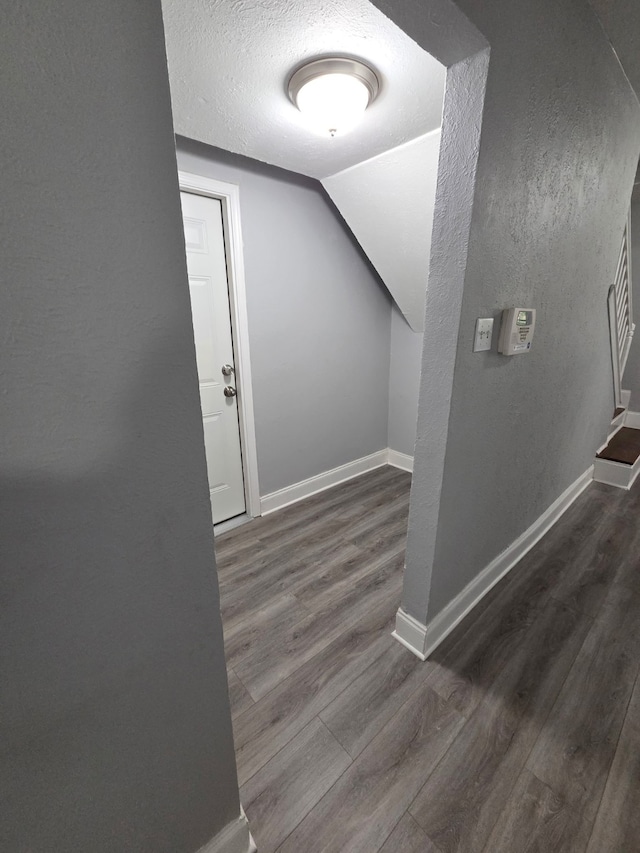 hallway with baseboards, a textured ceiling, wood finished floors, and lofted ceiling