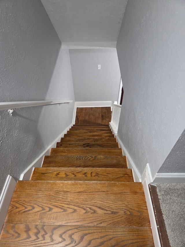 staircase with baseboards, a textured wall, and wood finished floors