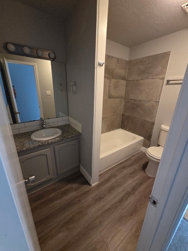 bathroom featuring vanity, wood finished floors, toilet, a textured ceiling, and  shower combination