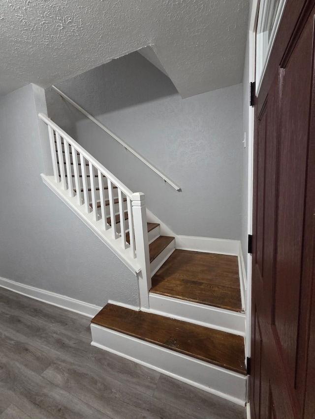 staircase featuring baseboards, a textured ceiling, and wood finished floors