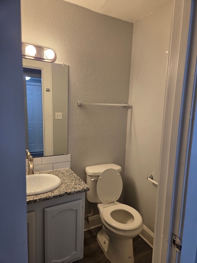 half bathroom with vanity, a textured wall, wood finished floors, and toilet