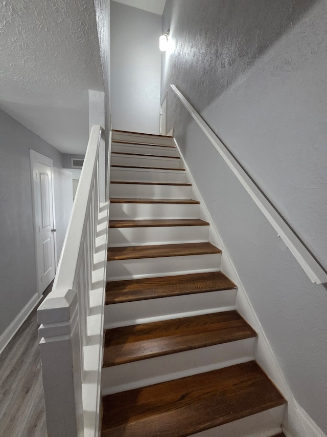 stairs featuring a textured ceiling, baseboards, and wood finished floors
