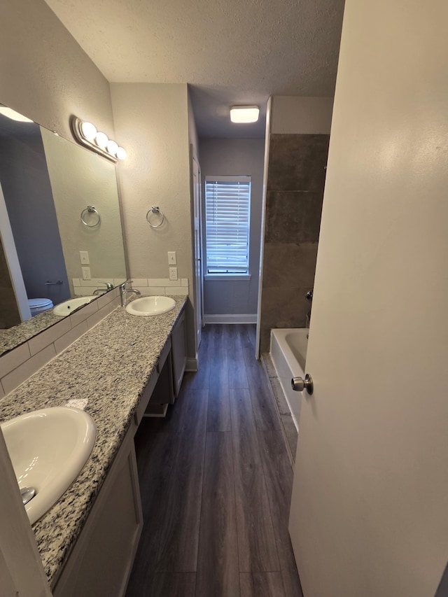 bathroom featuring a textured ceiling, a sink, a bath, and wood finished floors