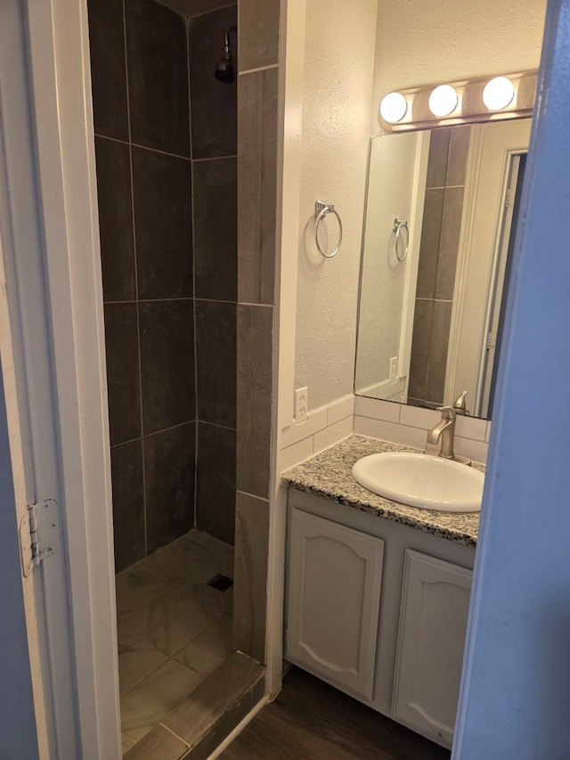 bathroom with vanity, a textured wall, a shower stall, and wood finished floors