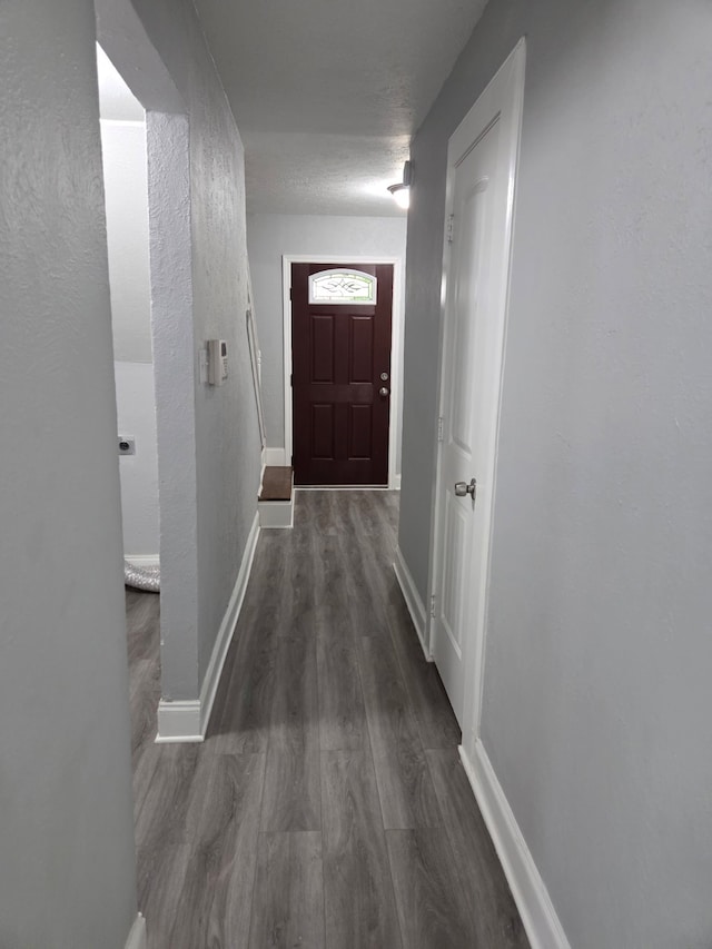 hallway featuring baseboards, dark wood-style flooring, and a textured wall