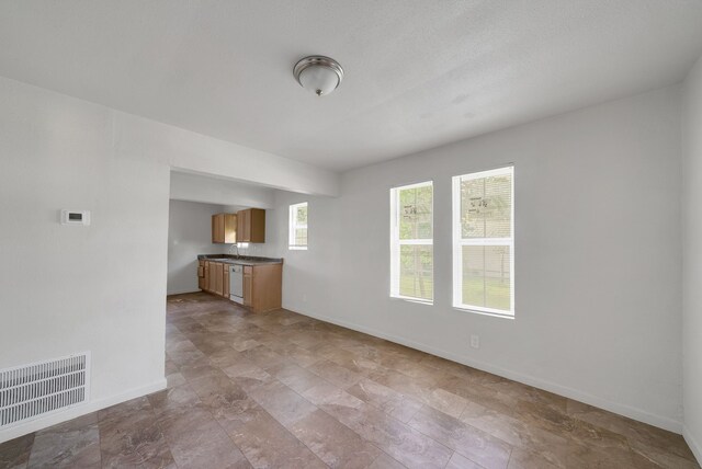 unfurnished living room with baseboards, visible vents, and a sink