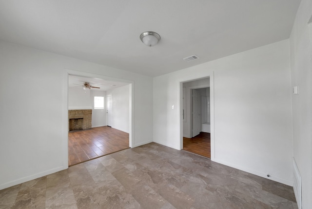 empty room with a brick fireplace, ceiling fan, visible vents, and baseboards