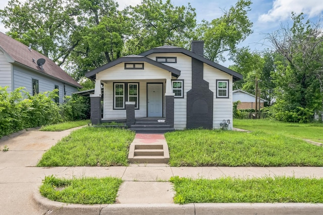 bungalow-style house featuring covered porch, a chimney, and a front yard