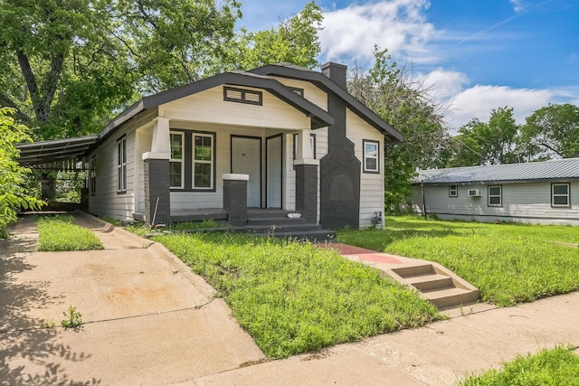 bungalow-style house featuring a porch, a front yard, a chimney, concrete driveway, and a carport