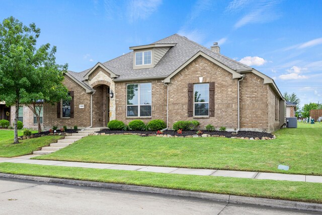 view of front of house with a front yard, cooling unit, a chimney, brick siding, and a shingled roof
