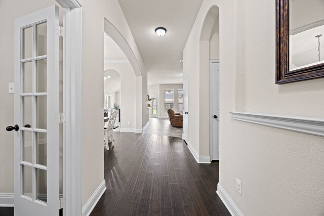 hall with baseboards, arched walkways, and dark wood-style floors