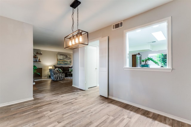 unfurnished dining area with visible vents, baseboards, wood finished floors, and an inviting chandelier