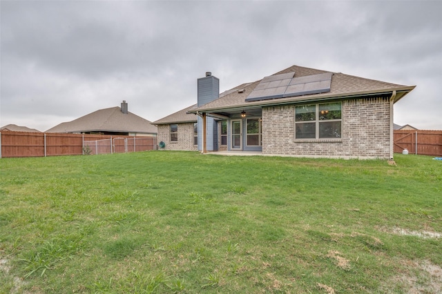 rear view of property with a chimney, a patio area, brick siding, roof mounted solar panels, and a fenced backyard