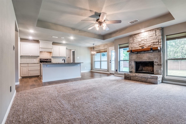unfurnished living room with baseboards, a ceiling fan, a tray ceiling, and visible vents