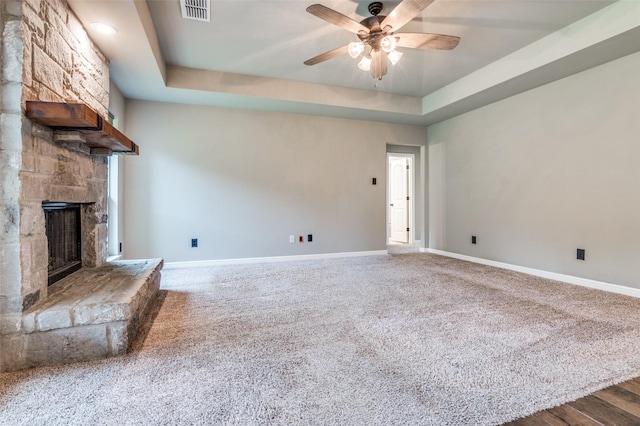 unfurnished living room featuring visible vents, a fireplace, baseboards, ceiling fan, and a tray ceiling