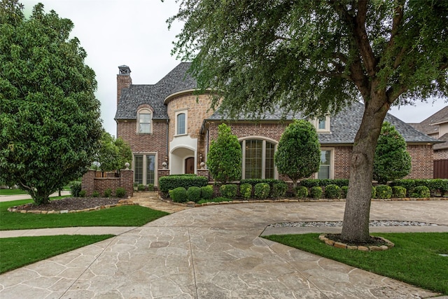 french country home with a high end roof, a front lawn, brick siding, a chimney, and curved driveway