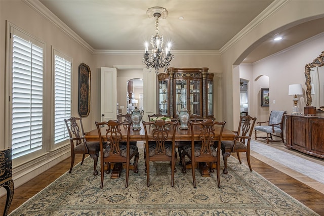 dining room with an inviting chandelier, arched walkways, wood finished floors, and ornamental molding