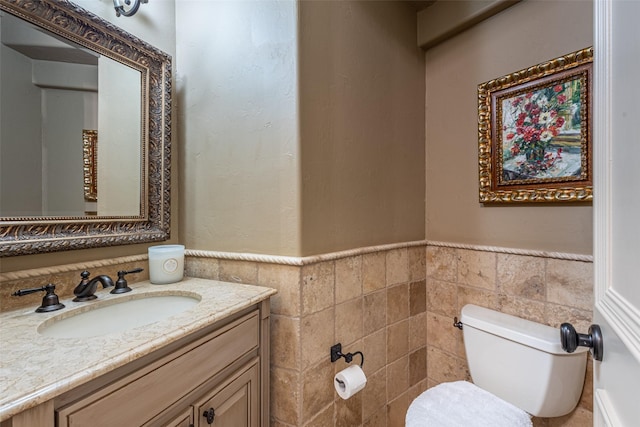 bathroom with vanity, wainscoting, toilet, and tile walls