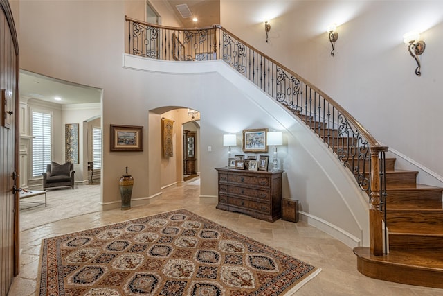 foyer entrance featuring arched walkways, a high ceiling, visible vents, and baseboards