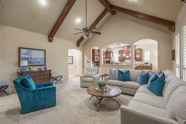 carpeted living room with arched walkways, baseboards, a ceiling fan, and beam ceiling